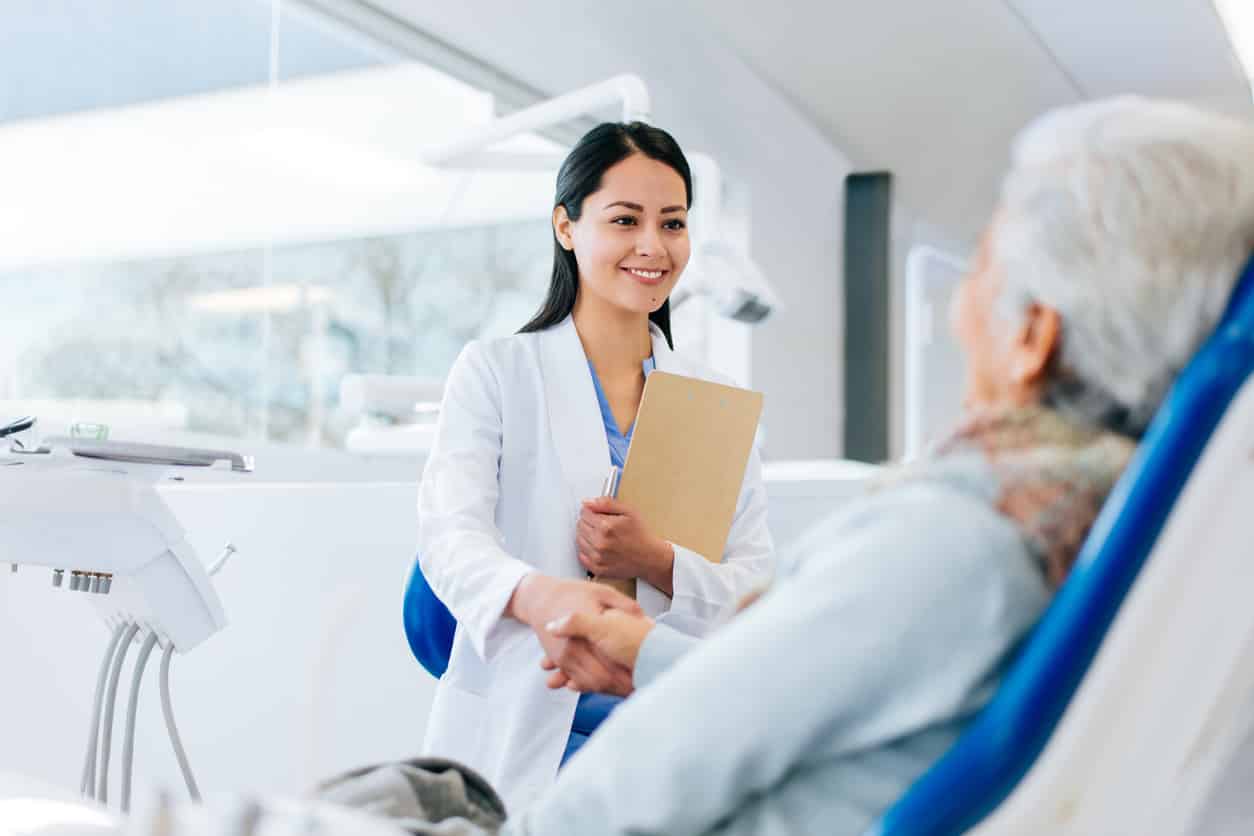 female dentist shaking hands with older woman in dentist chair