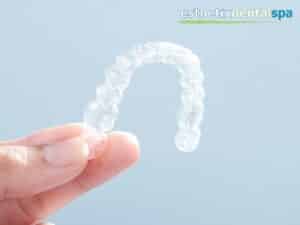 Hand holding clear aligners against a light blue background.